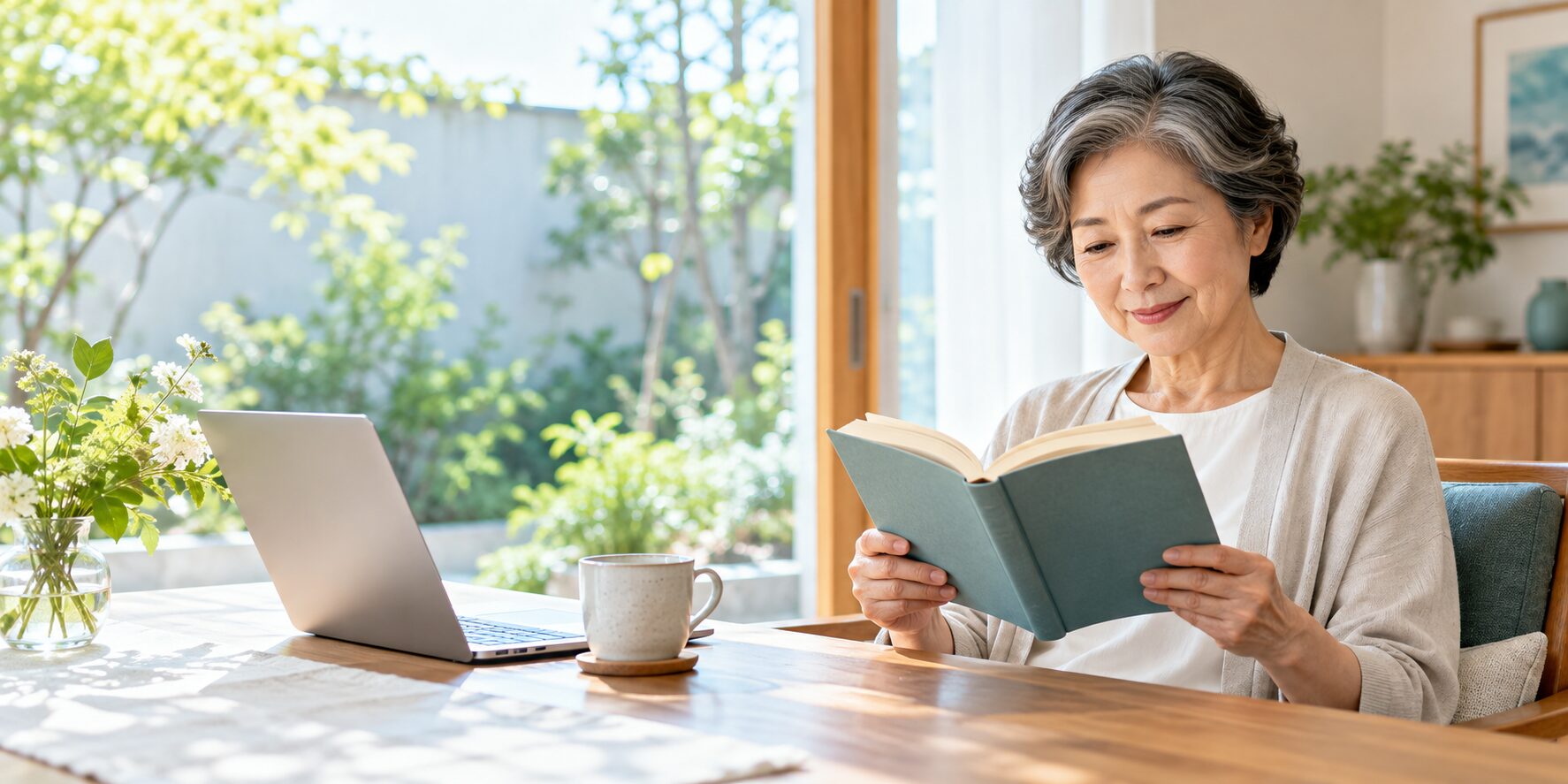 庭を眺められる窓辺で、パソコンをそばに置き、本を読む女性。遠方・中間・近方の生活場面